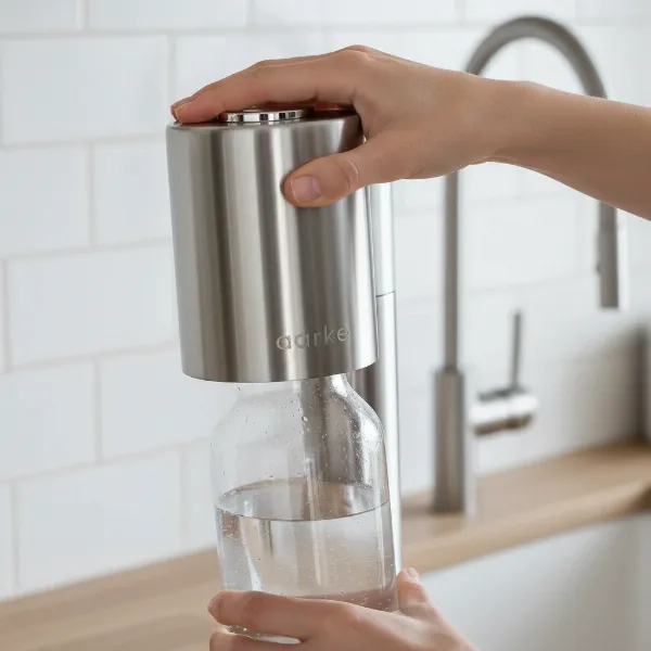 Person carbonating water using Aarke Carbonator Pro with its Push-to-Lock mechanism and glass bottle.